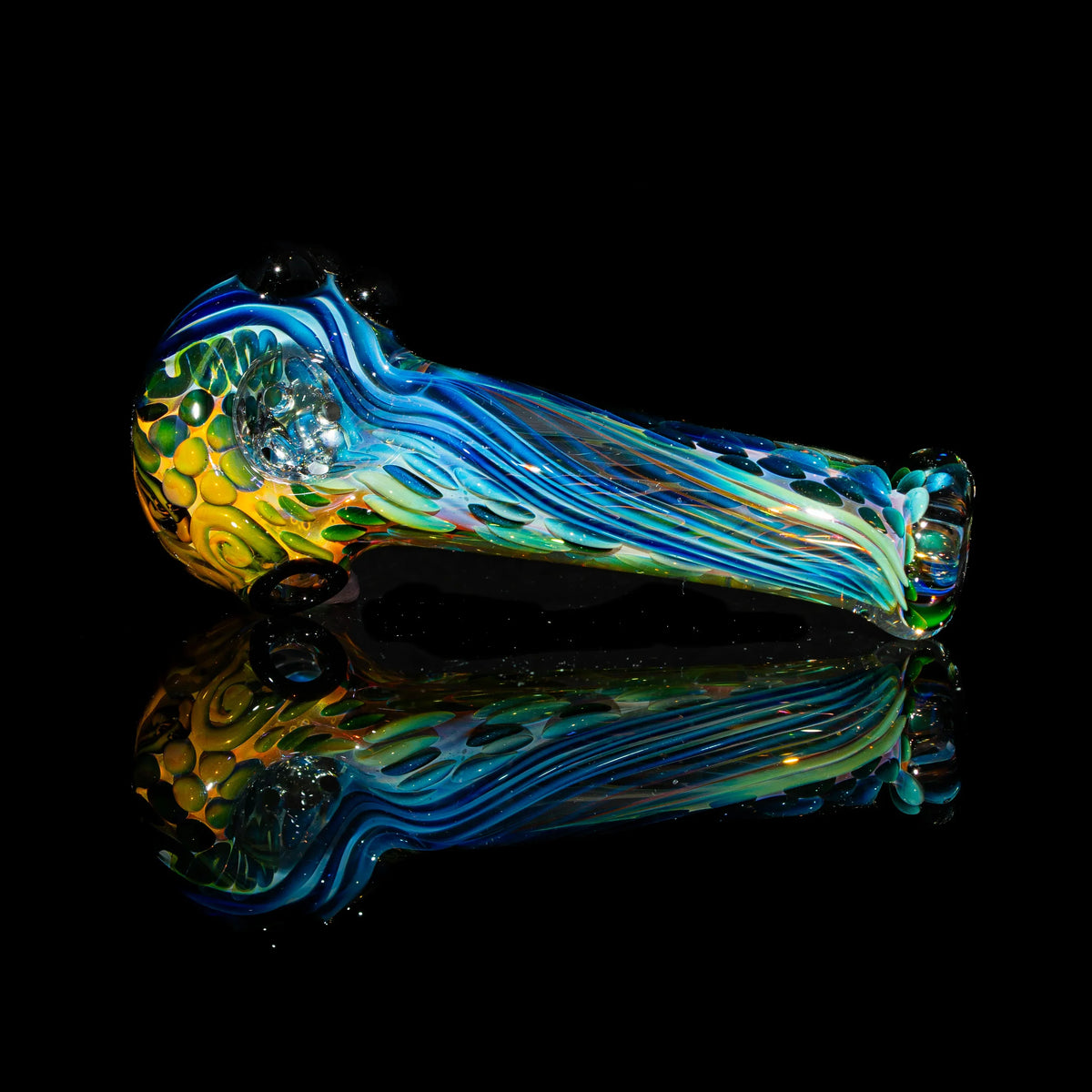 Colorful glass spoon pipe with blue, yellow, and green patterns on a black reflective surface