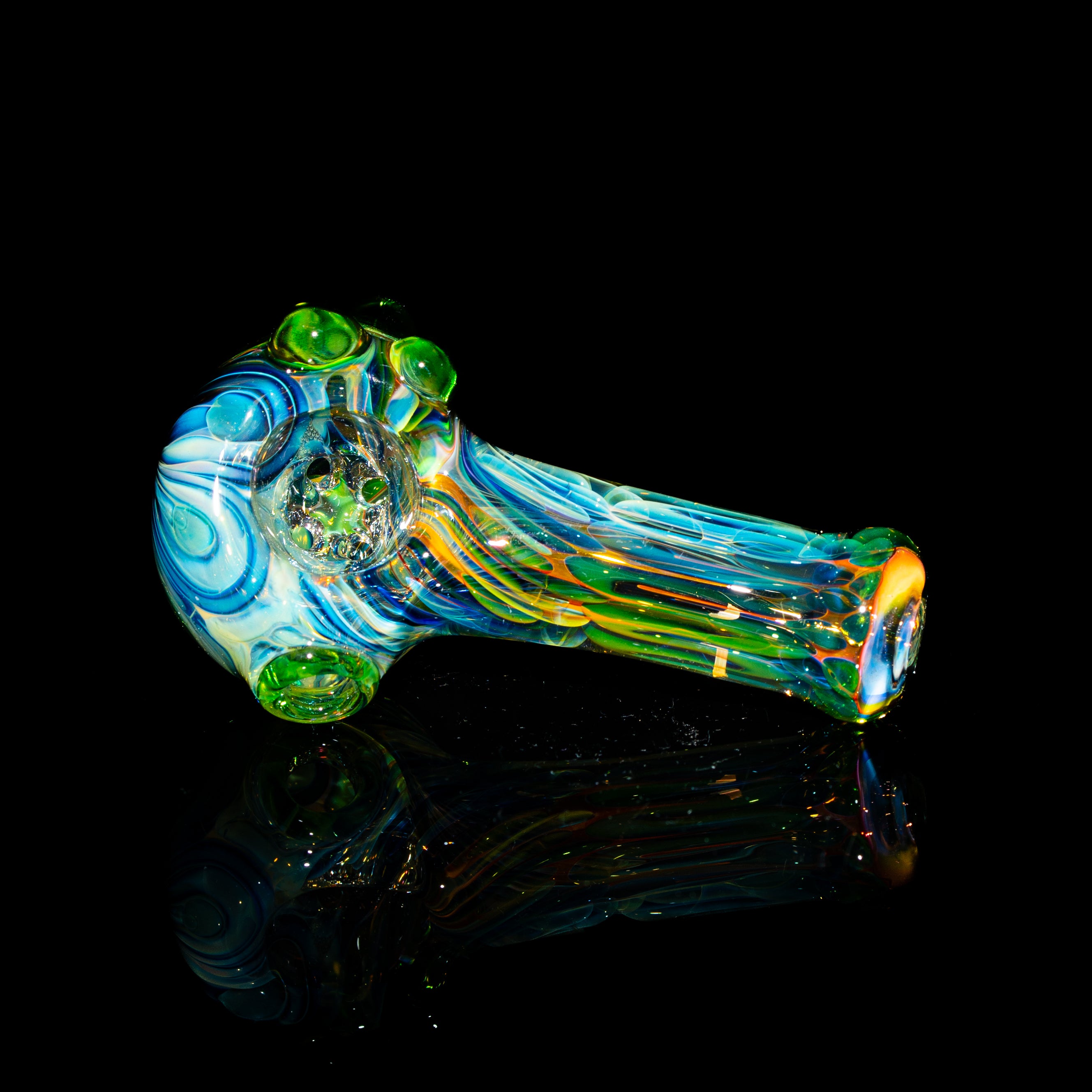 Colorful glass mini spoon pipe with green dots and four-hole design on black background.