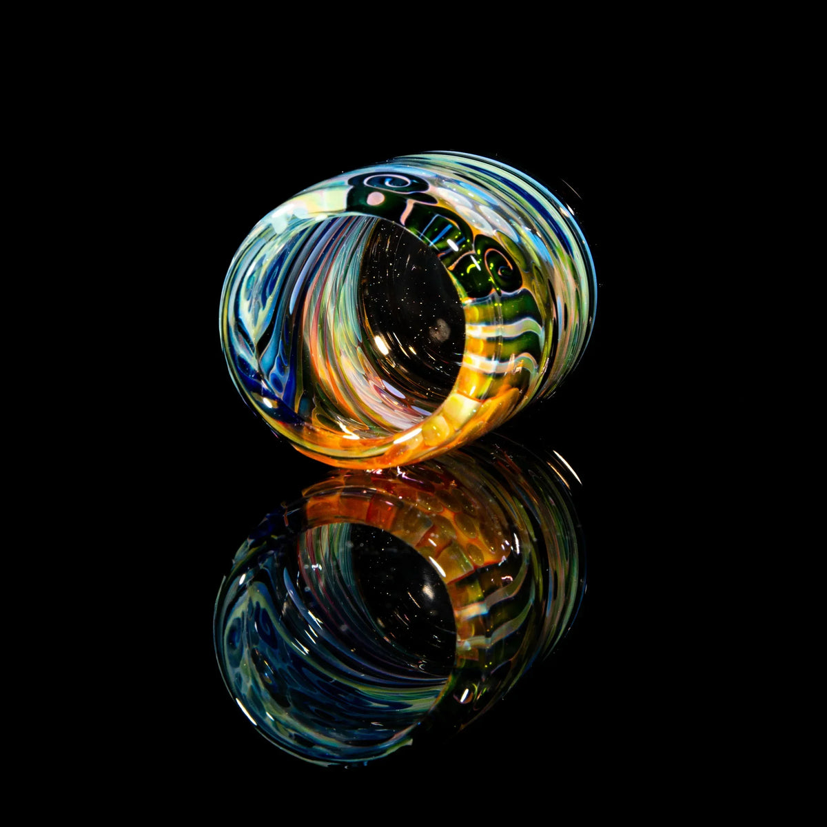 Colorful hand-blown glass jar with swirling patterns on a reflective black surface.