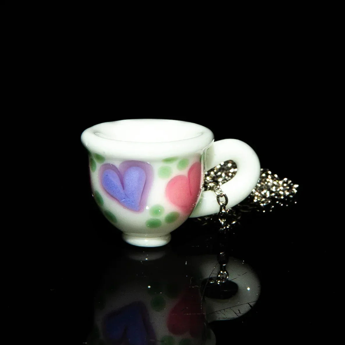 Glass tea cup pendant necklace with colorful heart designs and green dots on black background