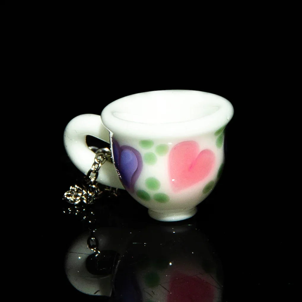Miniature glass teacup pendant with pink and purple hearts on chain, black background