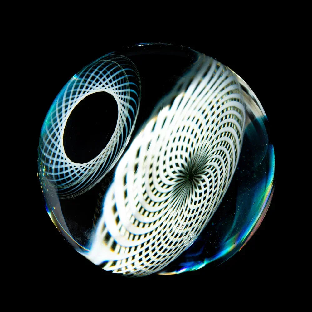 Handmade opal glass marble with intricate spiral white patterns on black background