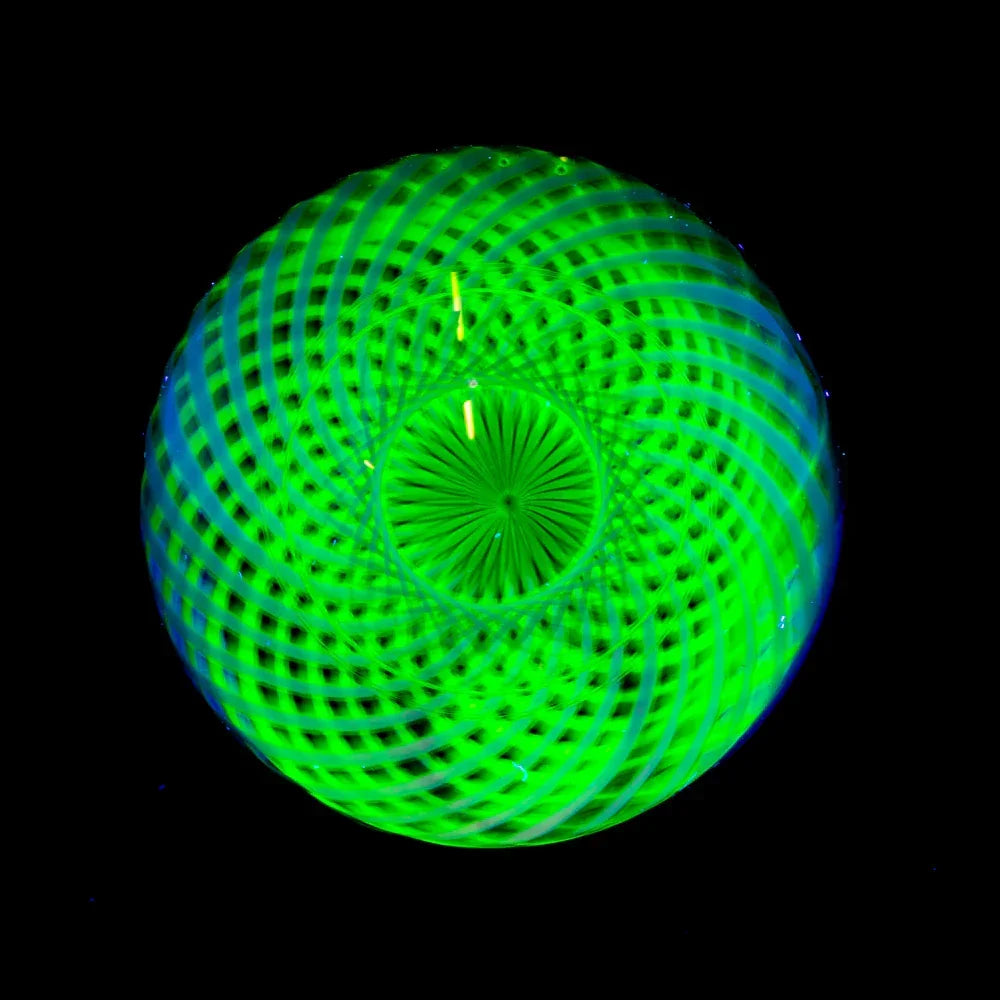Handcrafted glass marble with green spiral patterns and opal detail on black background