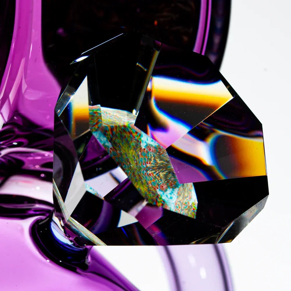 Close-up of a faceted glass gem with rainbow reflections and a purple glass background