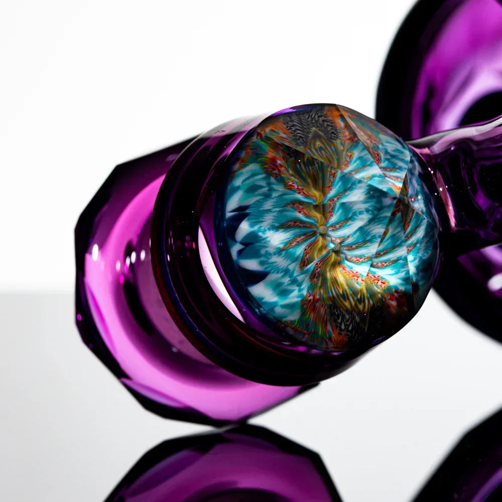 Close-up of a purple glass pipe with intricate colorful design on the base, reflective surface
