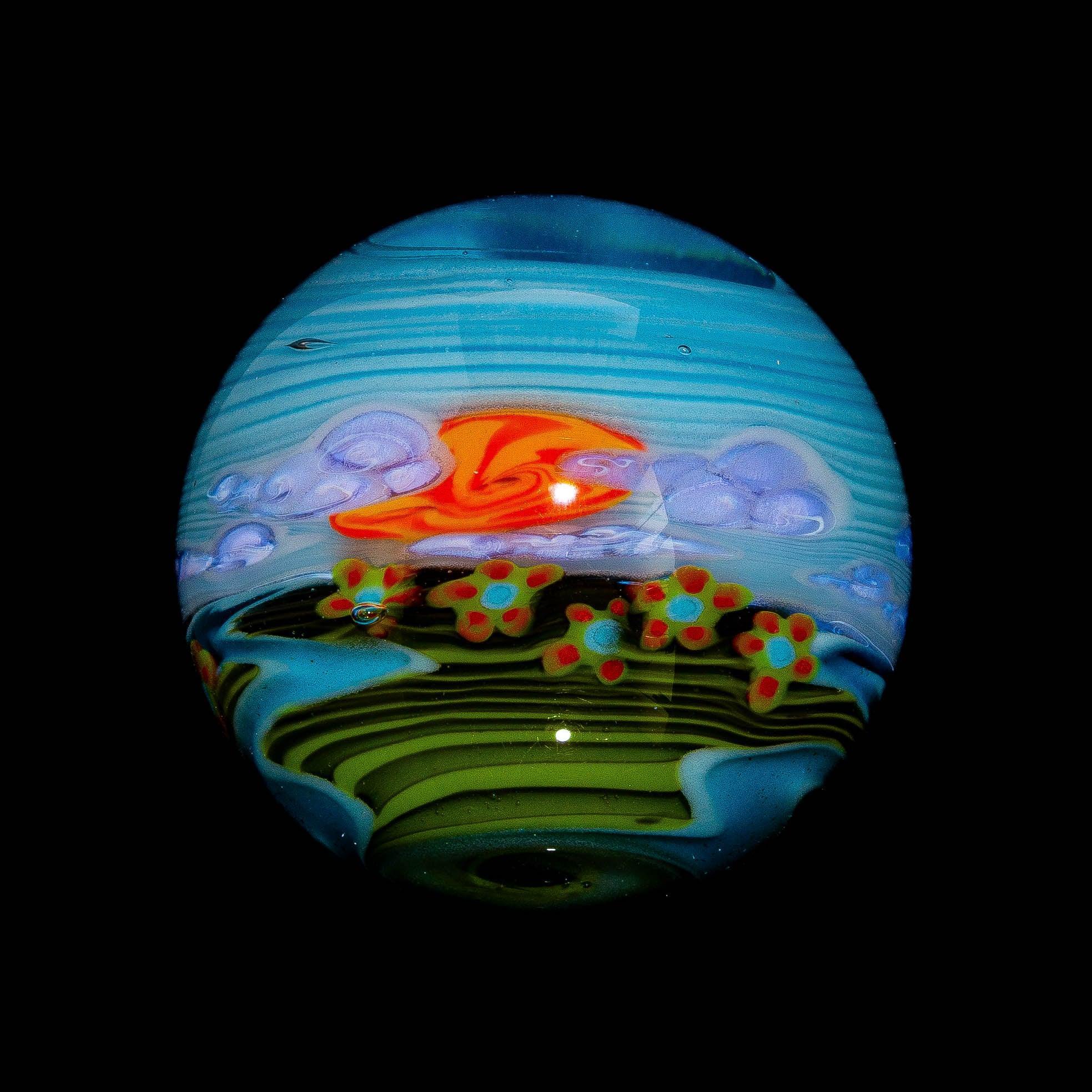 Colorful glass marble with abstract landscape, orange sun, blue sky, green fields, and flowers.