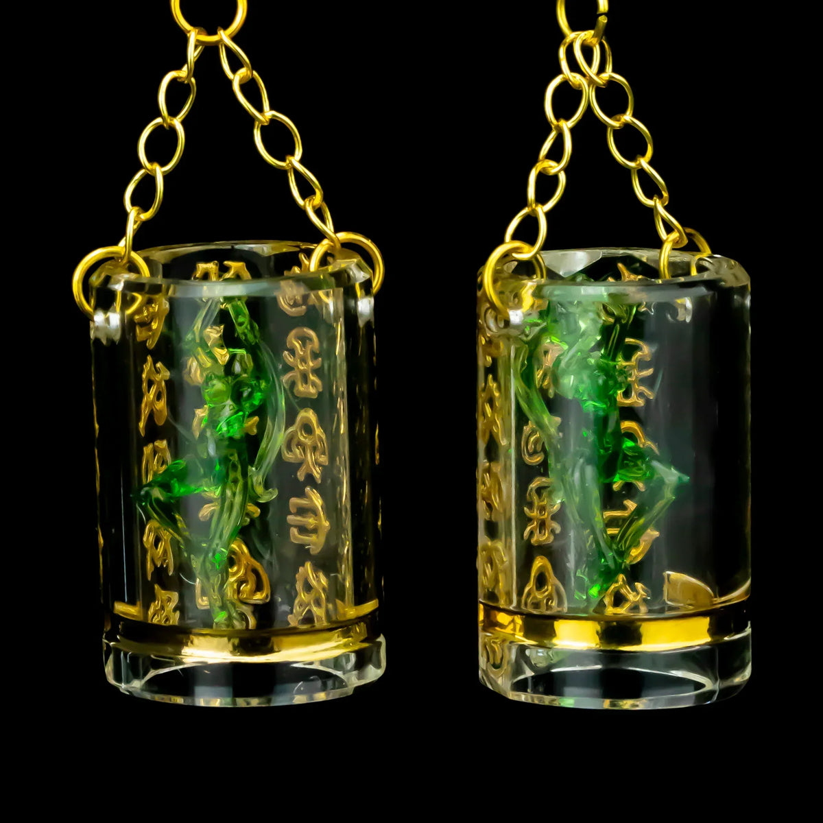 Glass earrings with gold calligraphy, green accents, and gold chain on black background