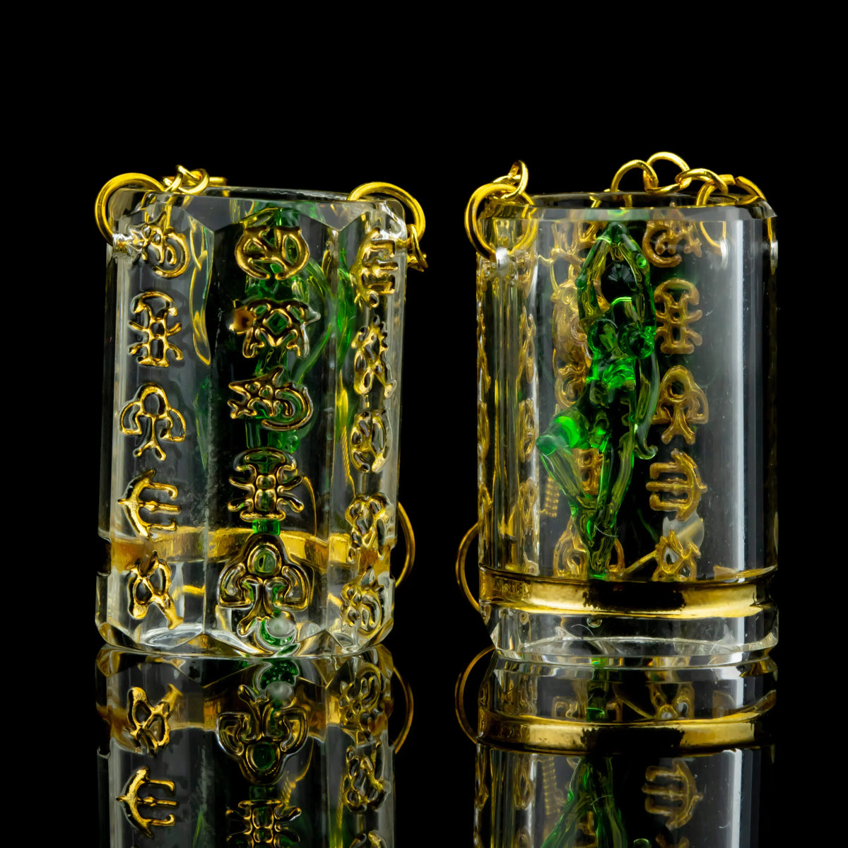 Clear and gold earrings with green glass detail, intricate script accents, reflective background