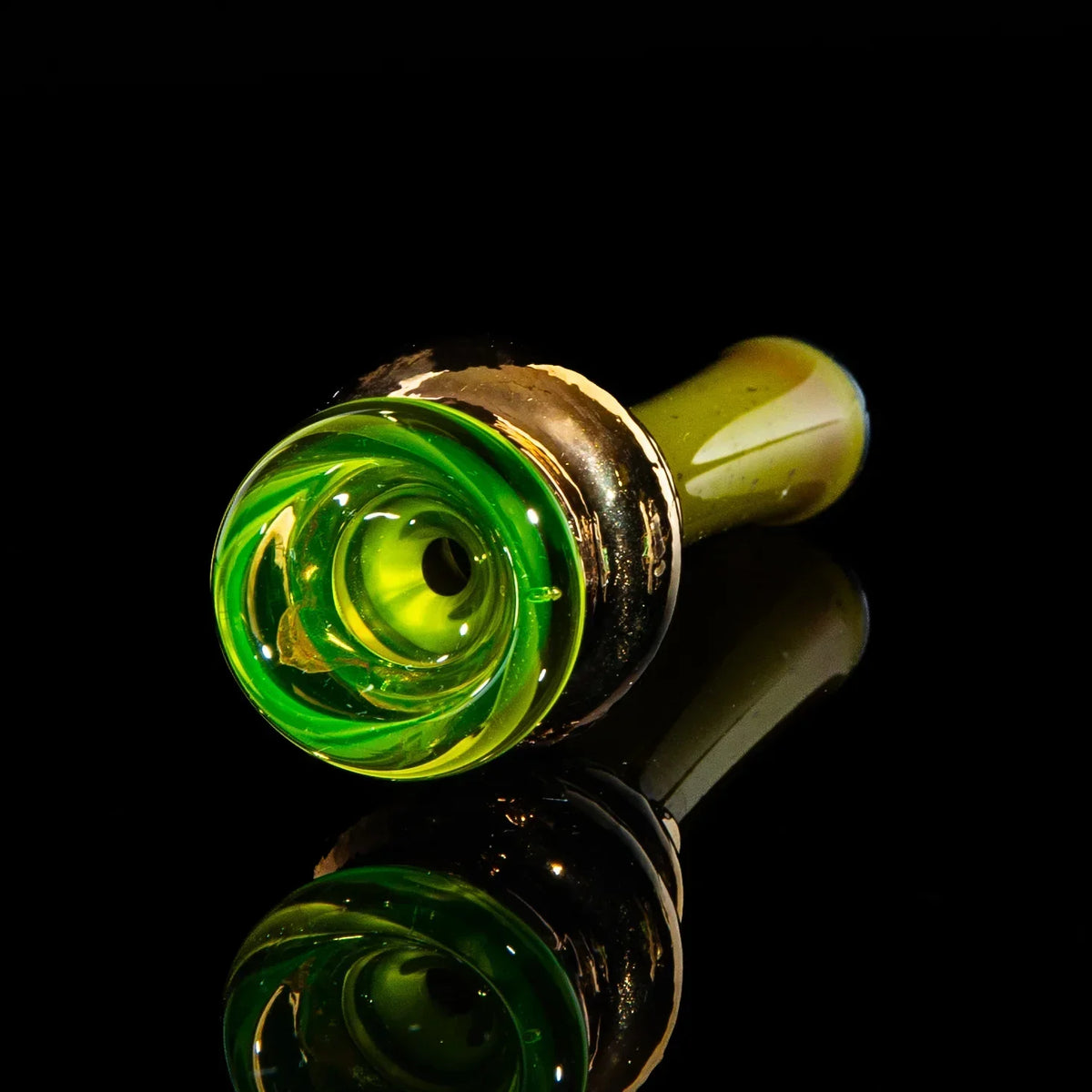 Hand-blown glass chillum with gold and green swirl design on a reflective black surface