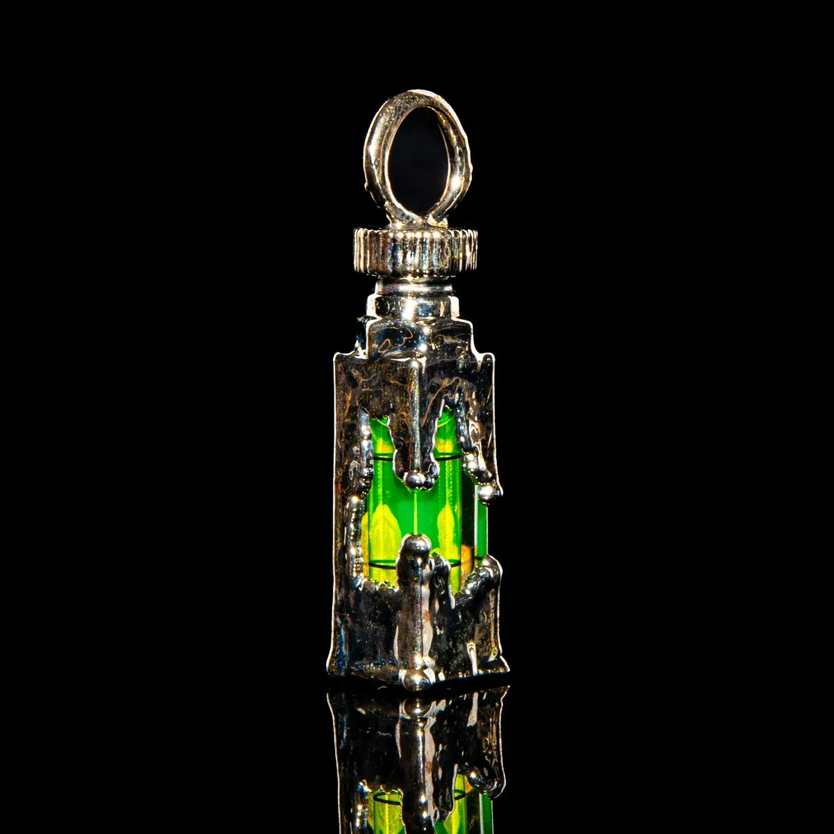 Handcrafted silver pendant with intricate design and neon green glass accent on black background.