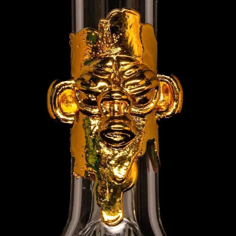 Close-up of a clear glass bong with a gold sculpted face accent on the neck