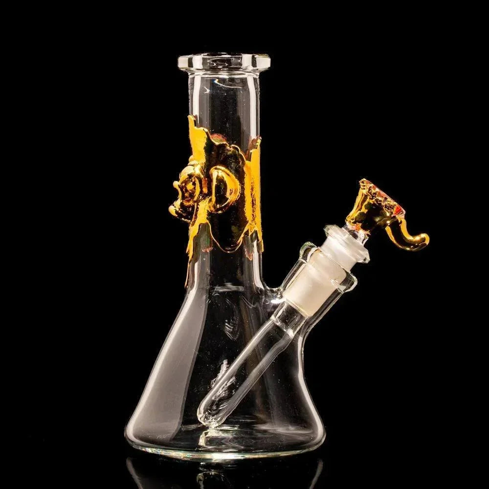 Clear glass beaker bong with gold accents and unique sculpted details on black background
