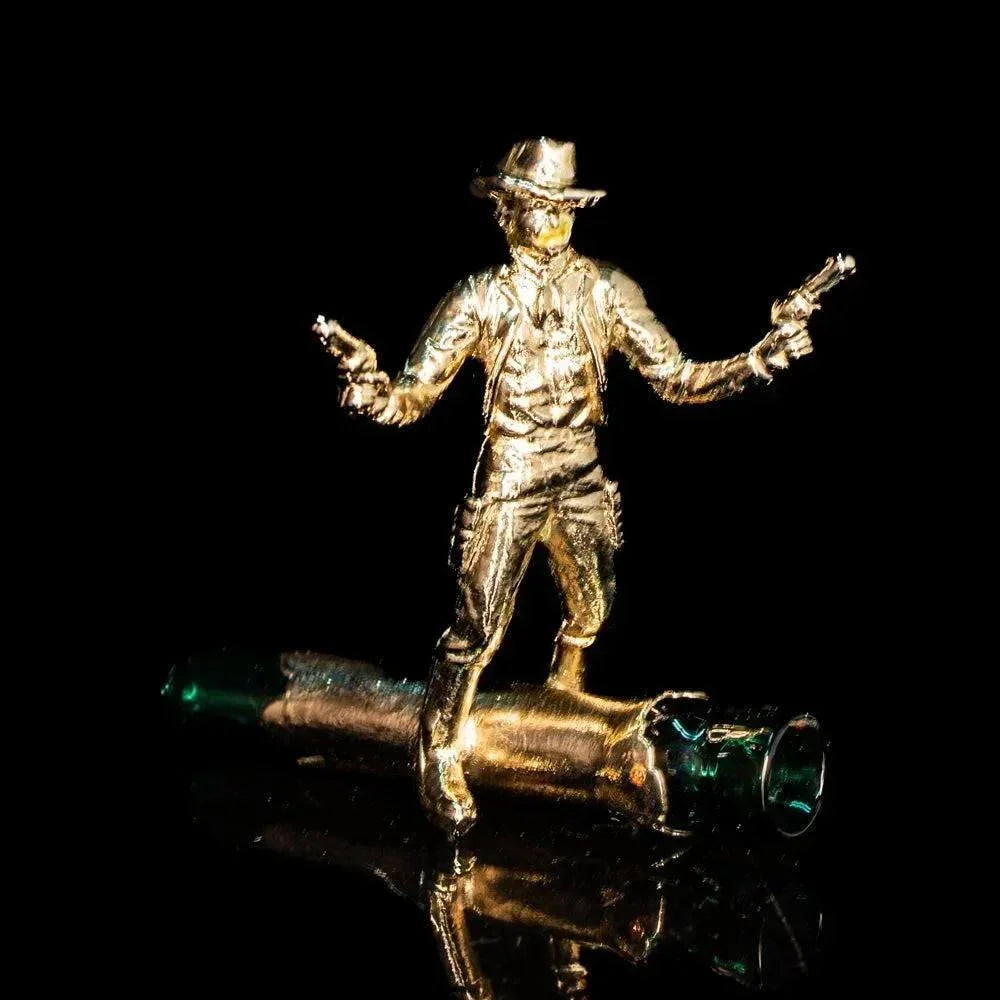 Gold cowboy figurine with dual pistols on a glass accessory against a black background