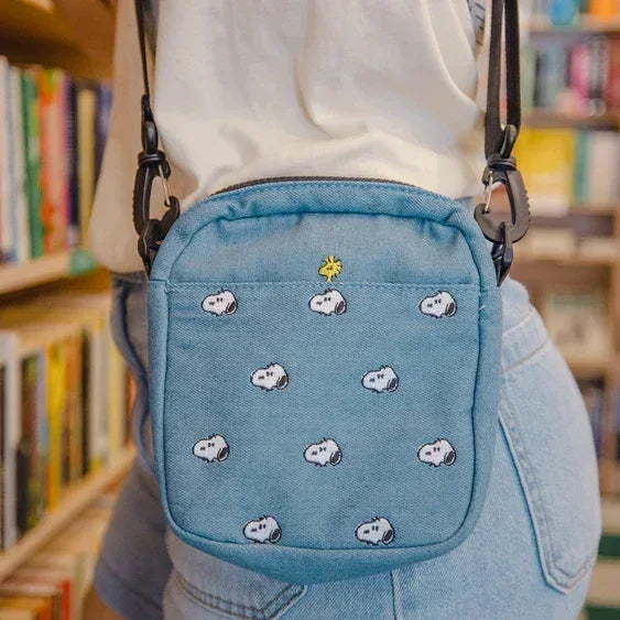 Light blue crossbody bag with embroidered cartoon characters, worn in a bookstore.