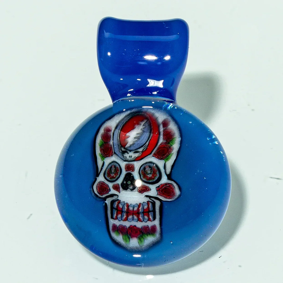 Blue glass pendant featuring a colorful skull with roses and lightning bolt design