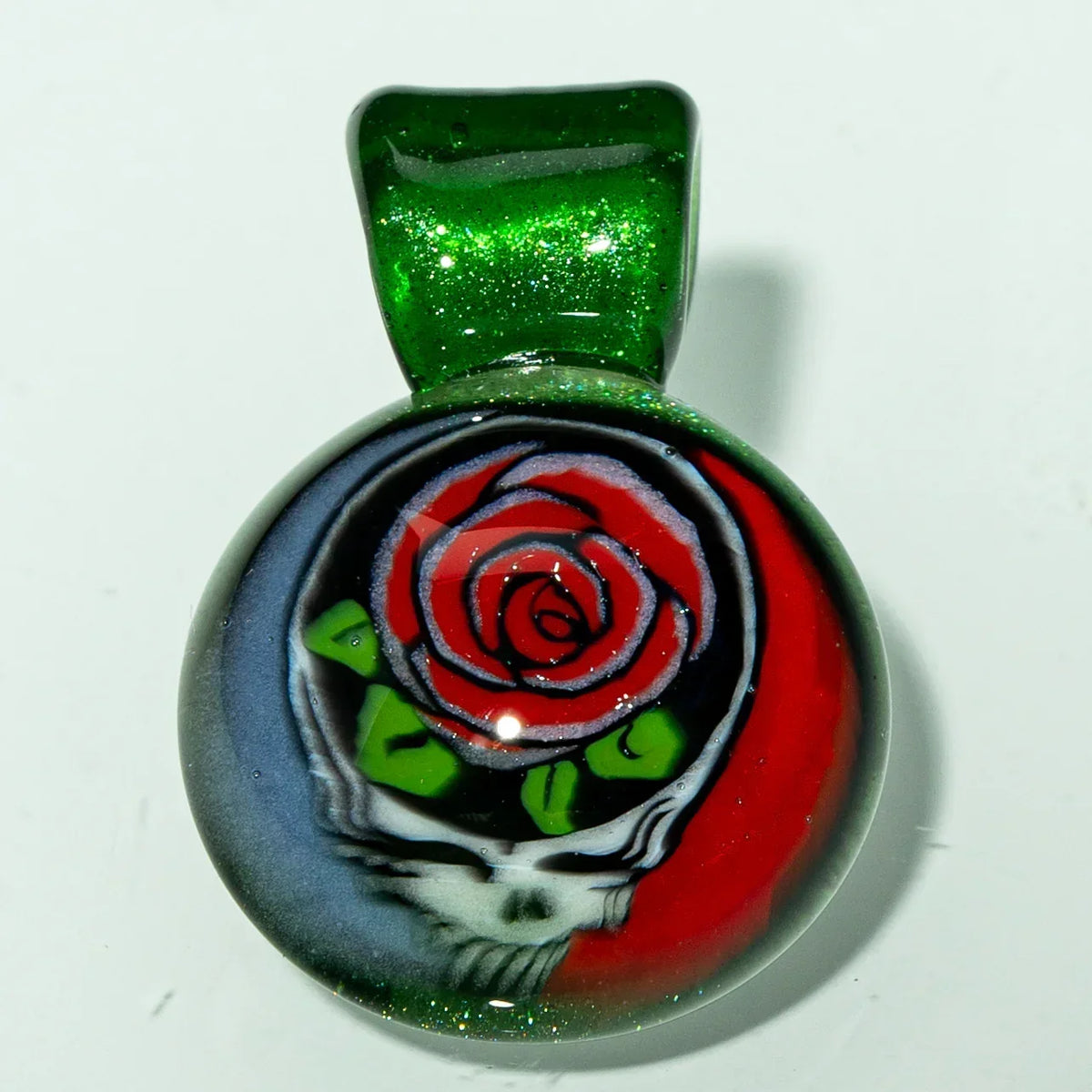Glass pendant with green bail, features skull and red rose design, smoke shop accessory.