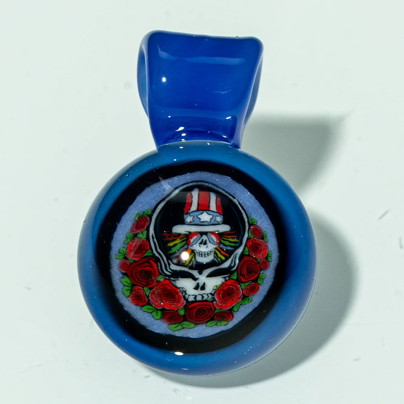 Blue glass pendant featuring a skull with roses and a red, white, and blue hat design