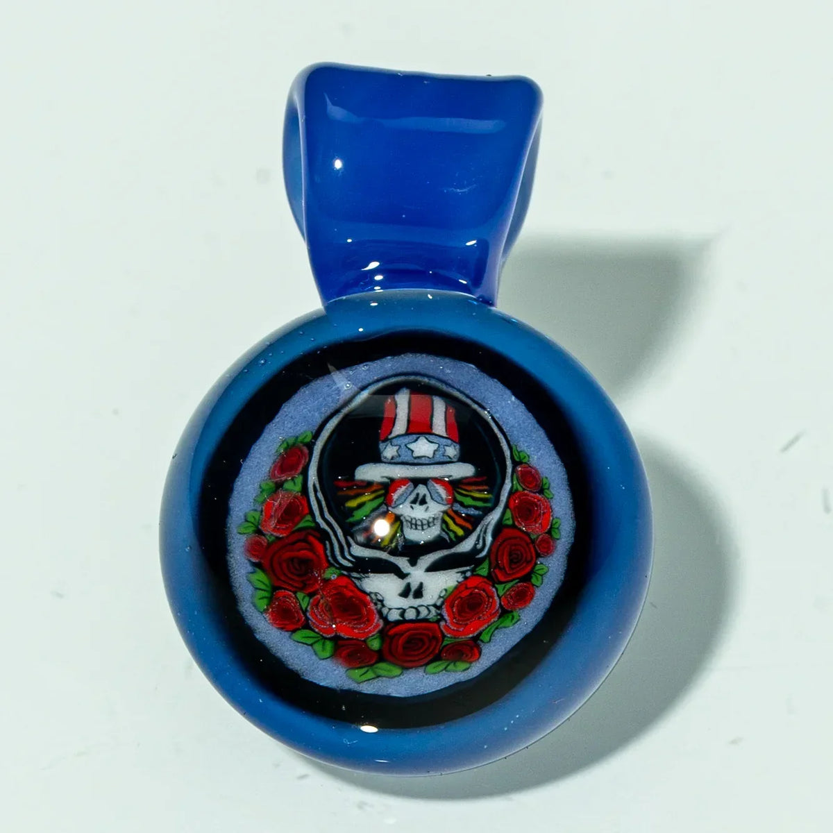 Blue glass pendant featuring a skull with roses and a red, white, and blue hat design