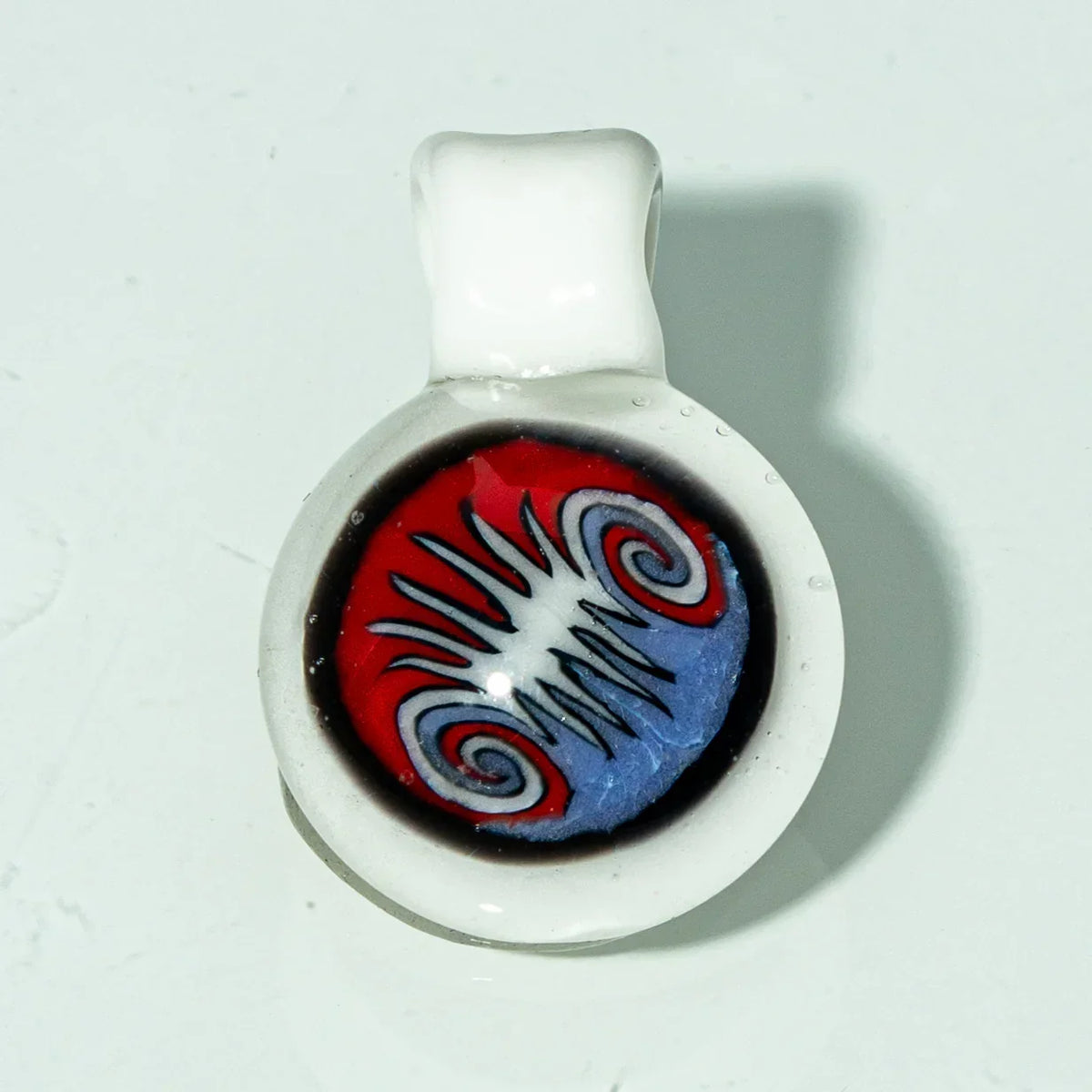 Handcrafted glass pendant with red, blue, and black swirled design on a white base