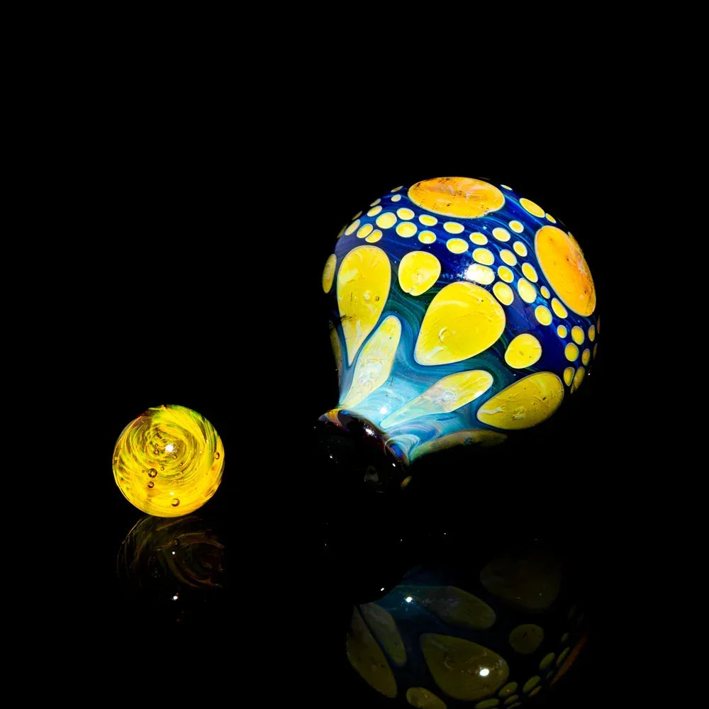 Colorful hand-blown glass carb cap and matching marble with yellow and blue patterns on black background