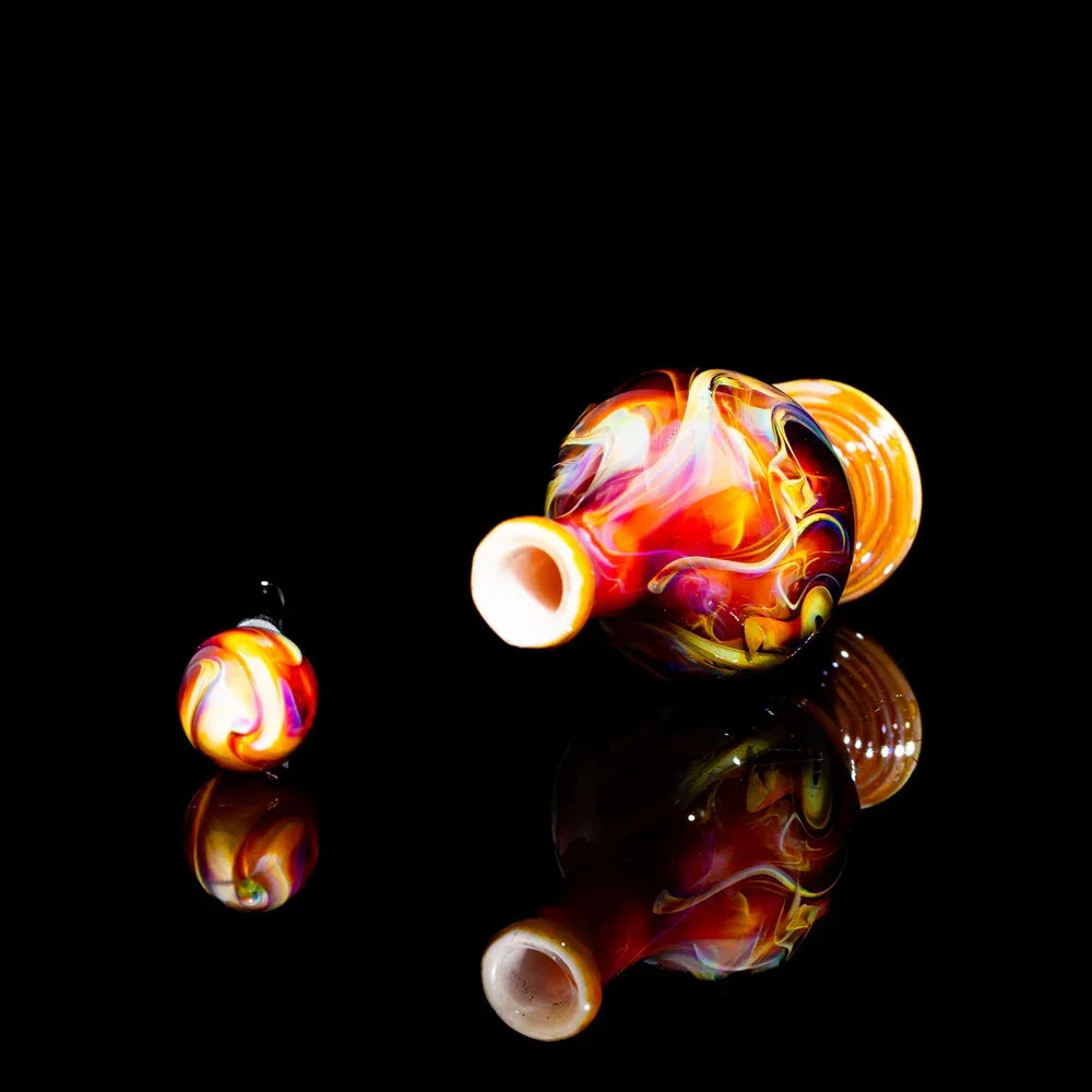 Colorful heady glass carb cap and marble set with swirling patterns on a black background