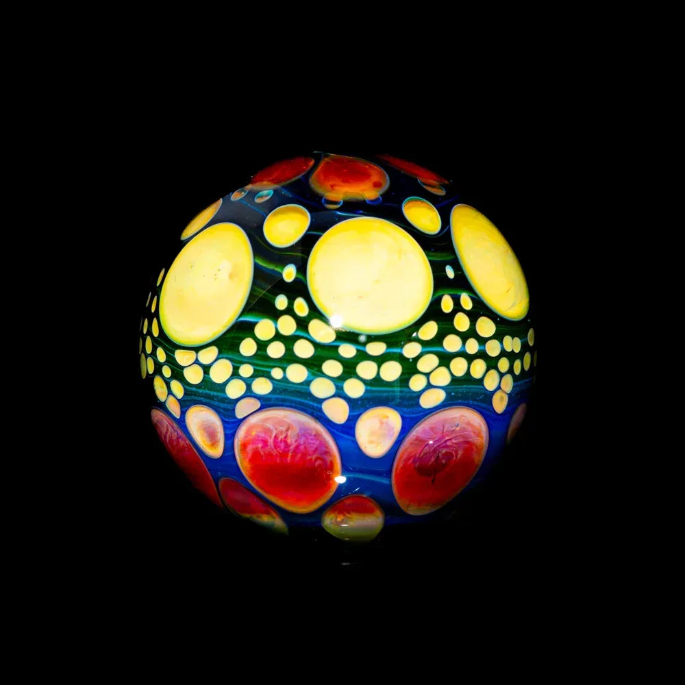 Hand-blown glass marble with colorful yellow, red, and blue dotted patterns on black background