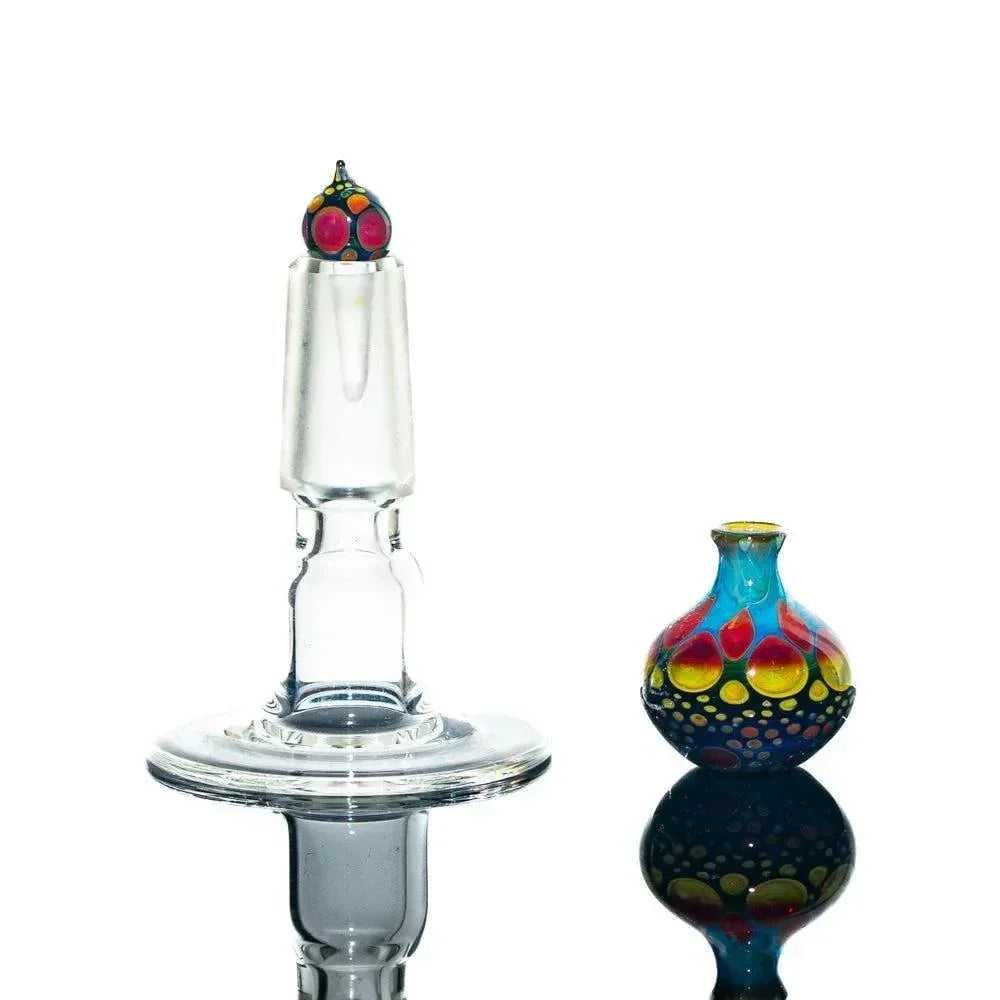 Colorful glass perfume jar with vibrant dots beside clear glass stand on white background
