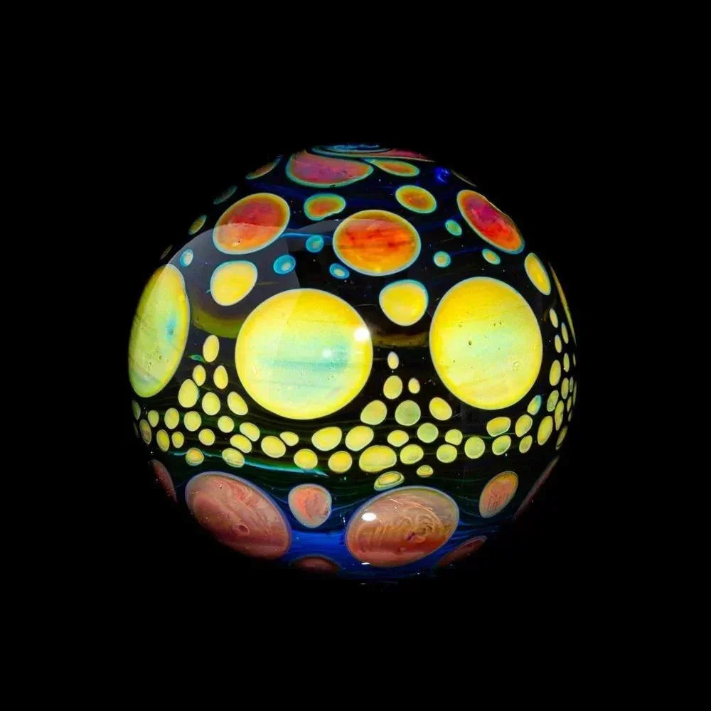 Colorful glass marble with yellow, orange, and blue hobnail dot pattern on black background
