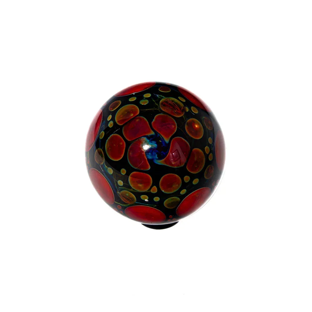 Handcrafted glass marble with red, yellow, and blue swirl dot patterns on black background