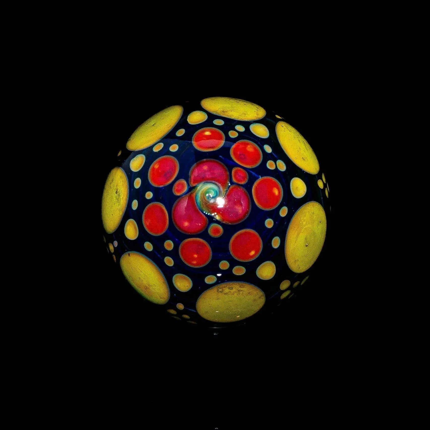 Blue glass marble with yellow and red hobnail dots on black background.