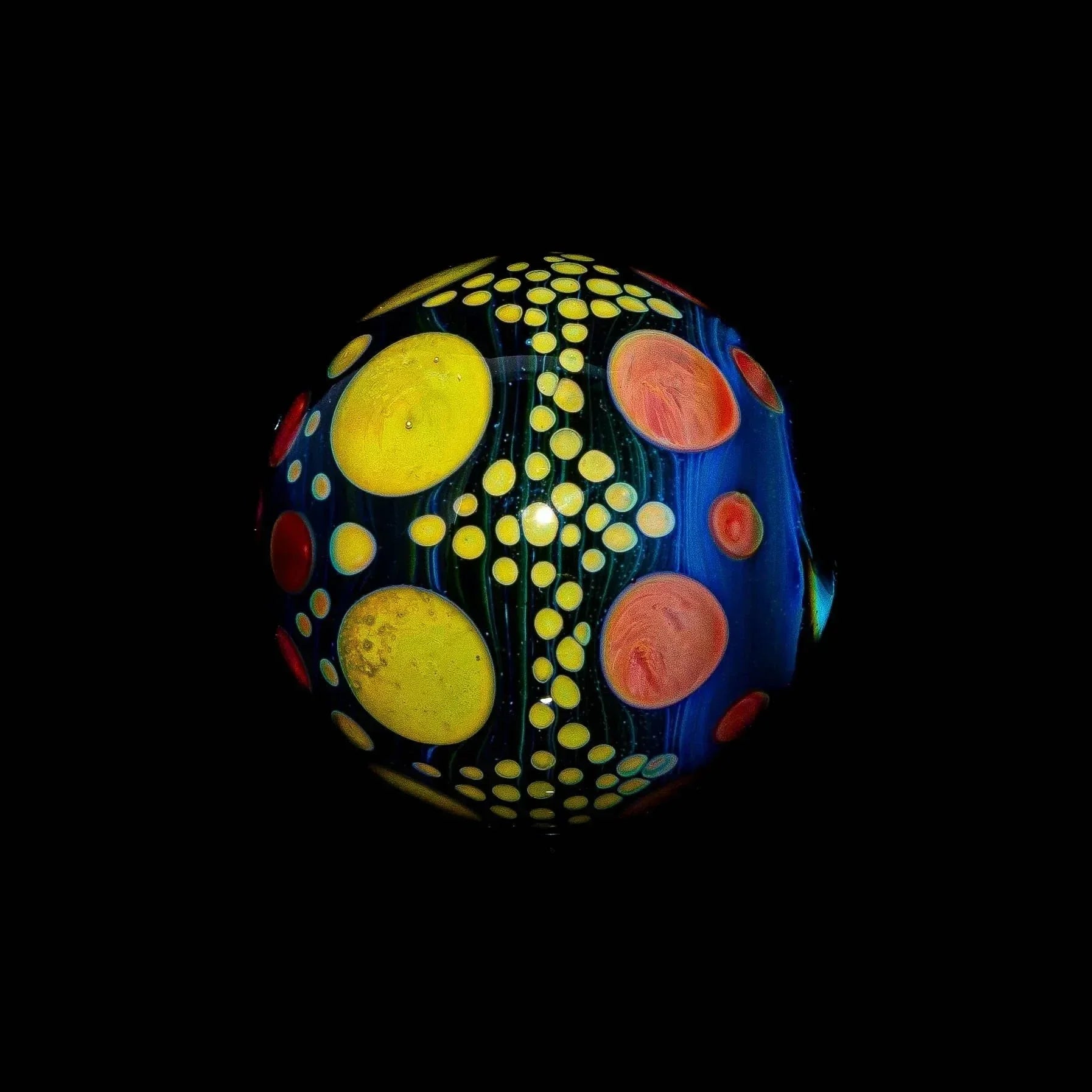 Colorful glass marble with blue, yellow, and red hobnail dot pattern on black background
