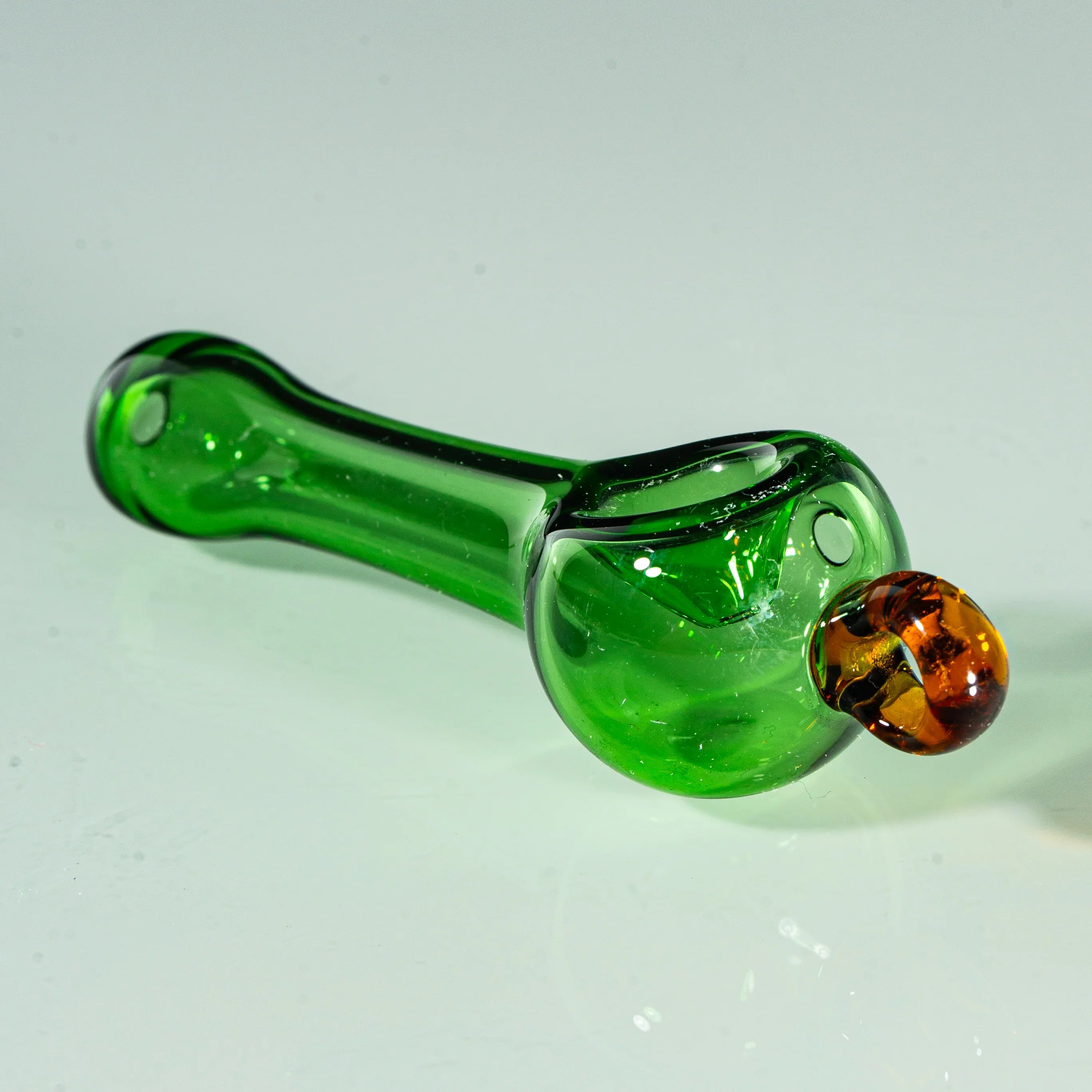 Transparent green glass hand pipe with amber accent for smoking, displayed on white surface