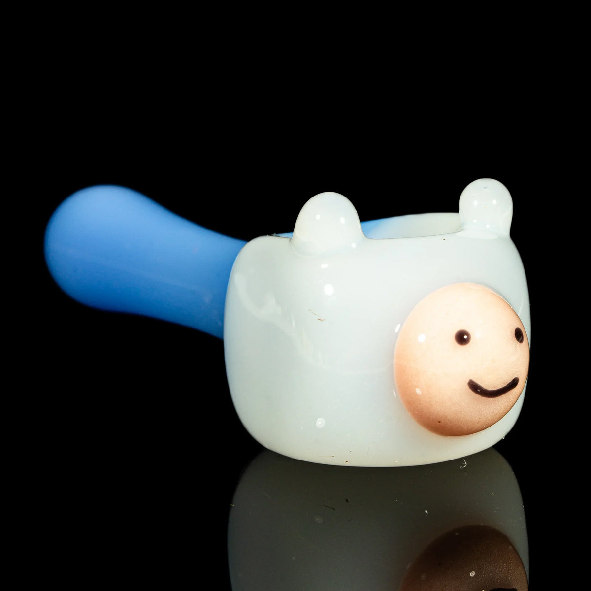 Hand-blown glass spoon pipe with cartoon face, white bowl and blue handle, on black background