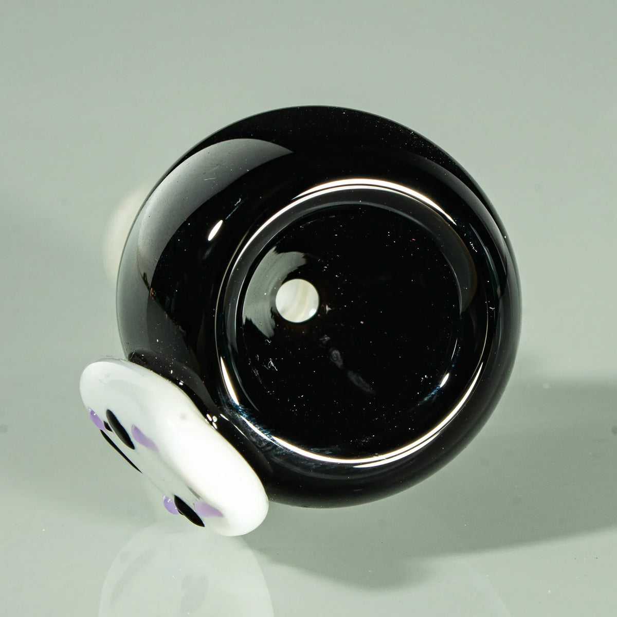 Black glass 14mm slide bowl with white and purple face accent, on reflective surface