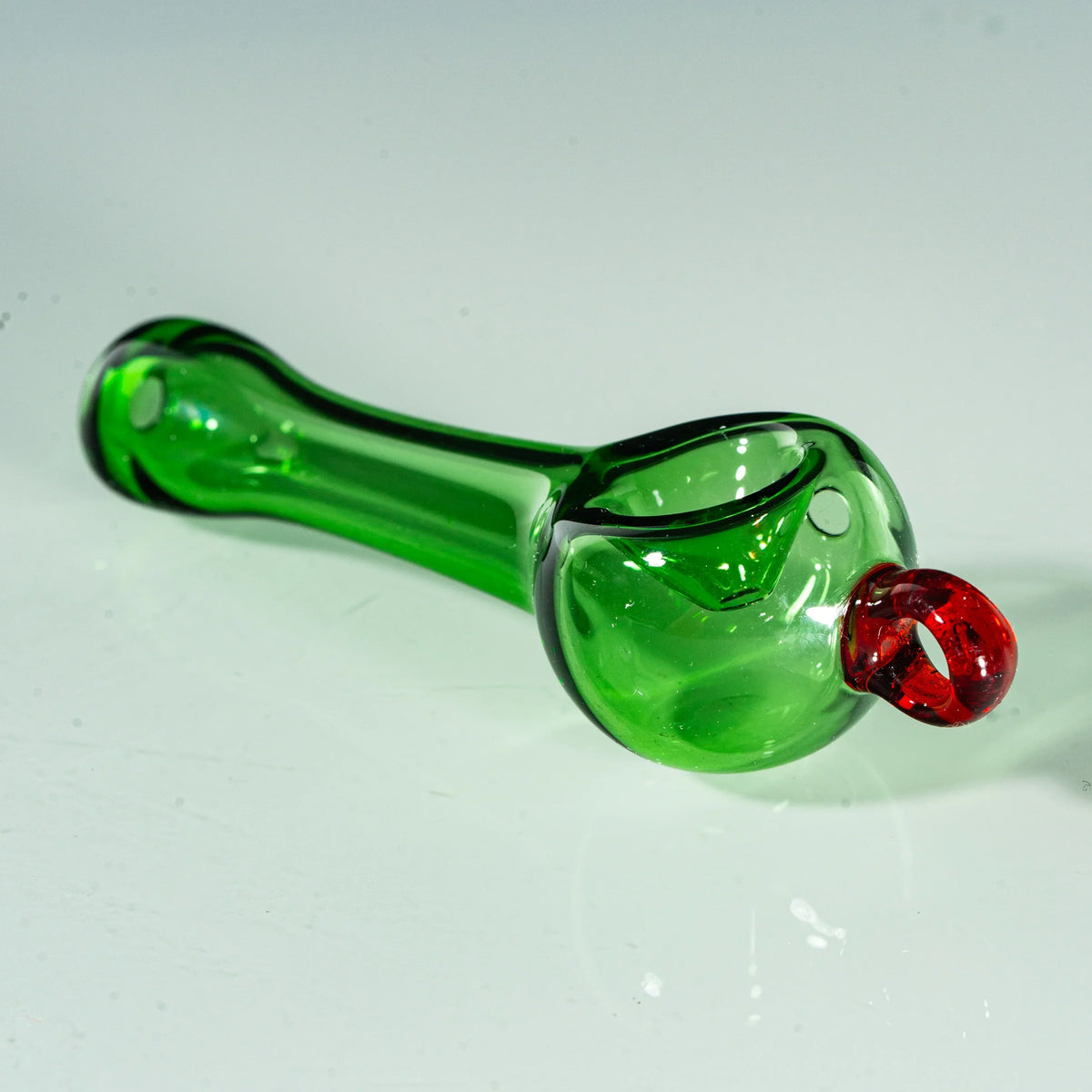 Green glass hand pipe with red accent, transparent spoon shape on white background