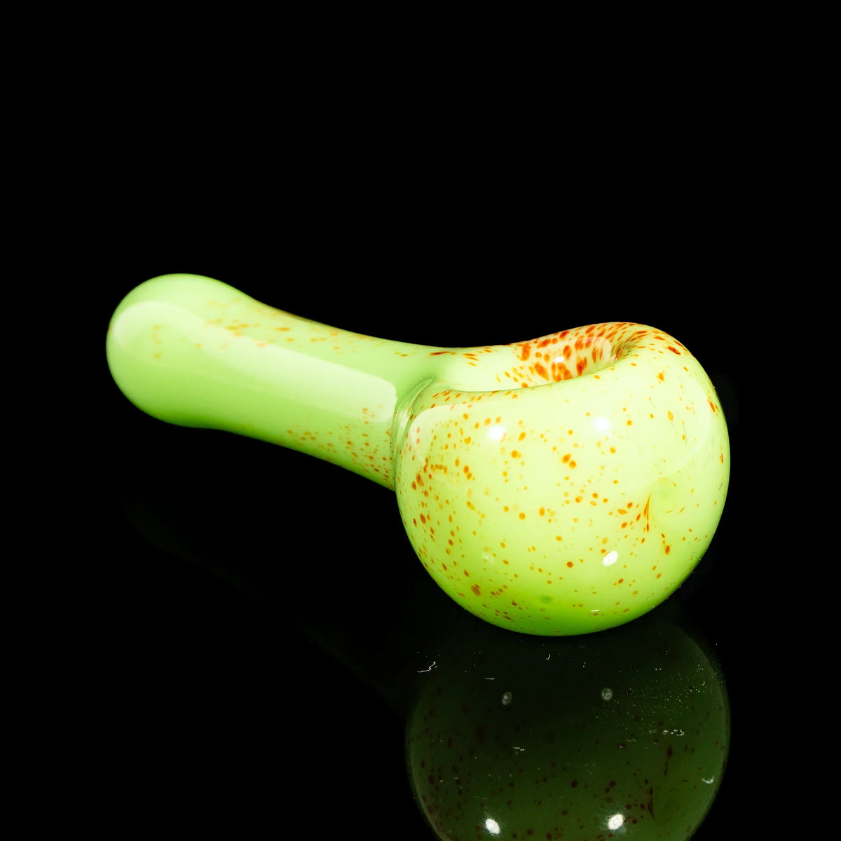 Green glass hand pipe with orange splatter design on a glossy black background