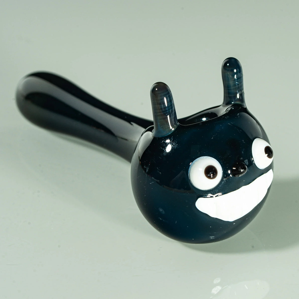 Totoro-inspired black glass hand pipe with cartoon face, white eyes, and big smile