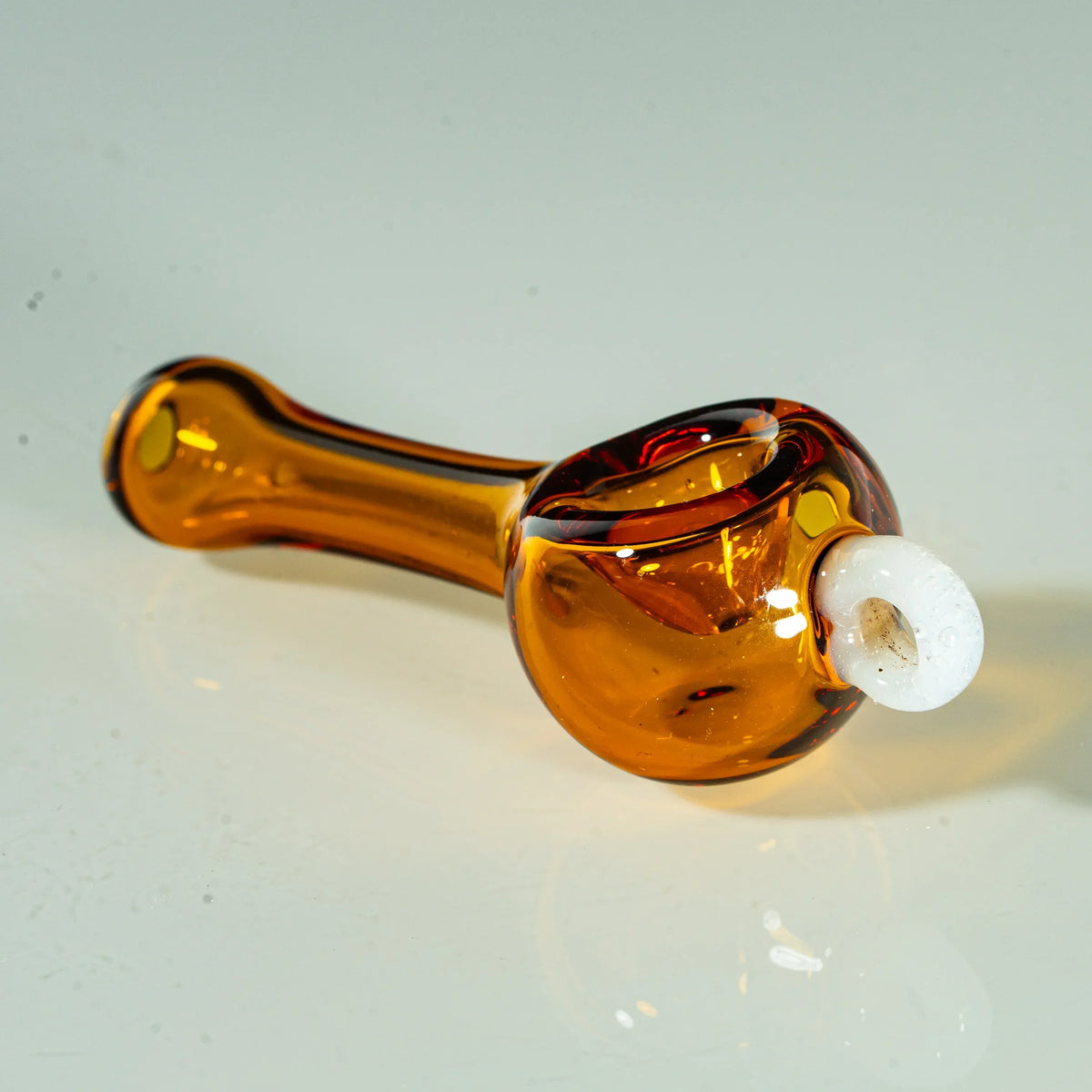 Amber glass hand pipe with white marble accent, displayed on a reflective surface