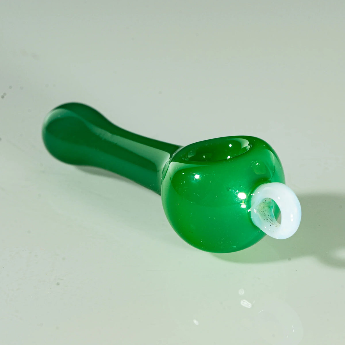 Green glass spoon pipe with white bailed accent, displayed on a light background