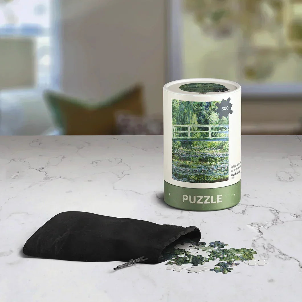 300-piece bridge garden puzzle in round container with puzzle pieces and drawstring bag on marble table
