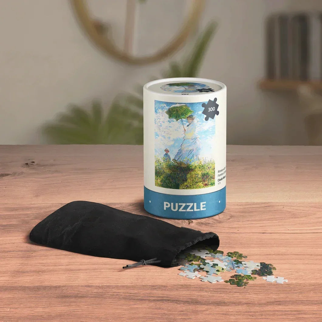300 piece art puzzle in cylindrical box with black pouch and pieces on wooden table