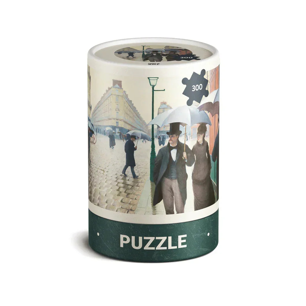 300 piece puzzle in a round box featuring a Paris street scene with people holding umbrellas