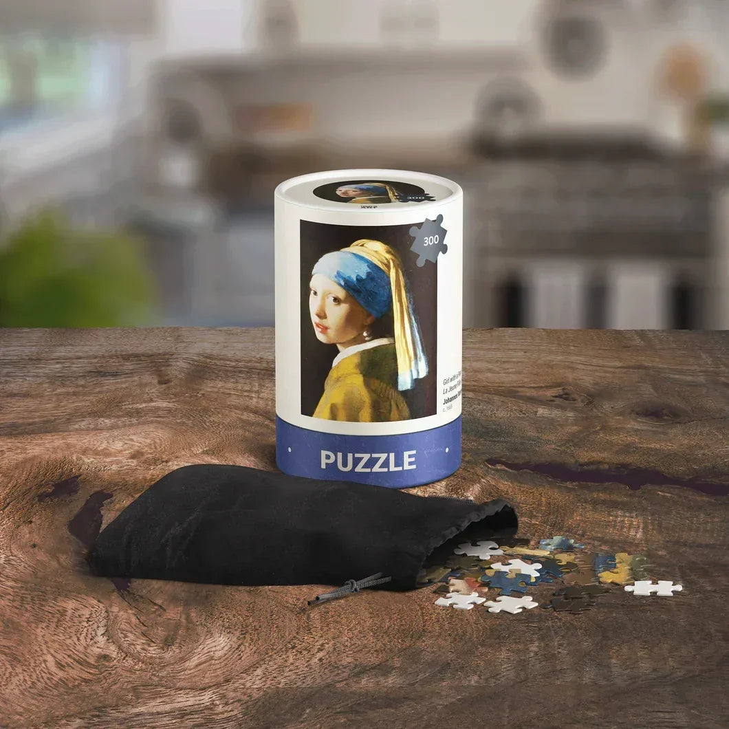300-piece Girl with a Pearl Earring puzzle in cylindrical box with loose pieces on wooden table