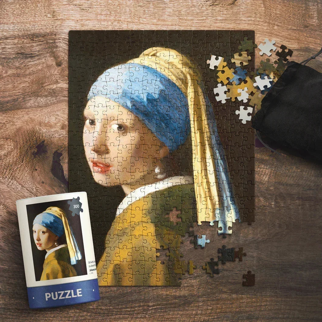Girl with a Pearl Earring art puzzle on wooden table, loose pieces and puzzle box visible.