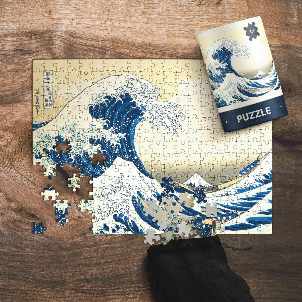 Person assembling a 300-piece puzzle of Hokusai's Great Wave on a wooden table