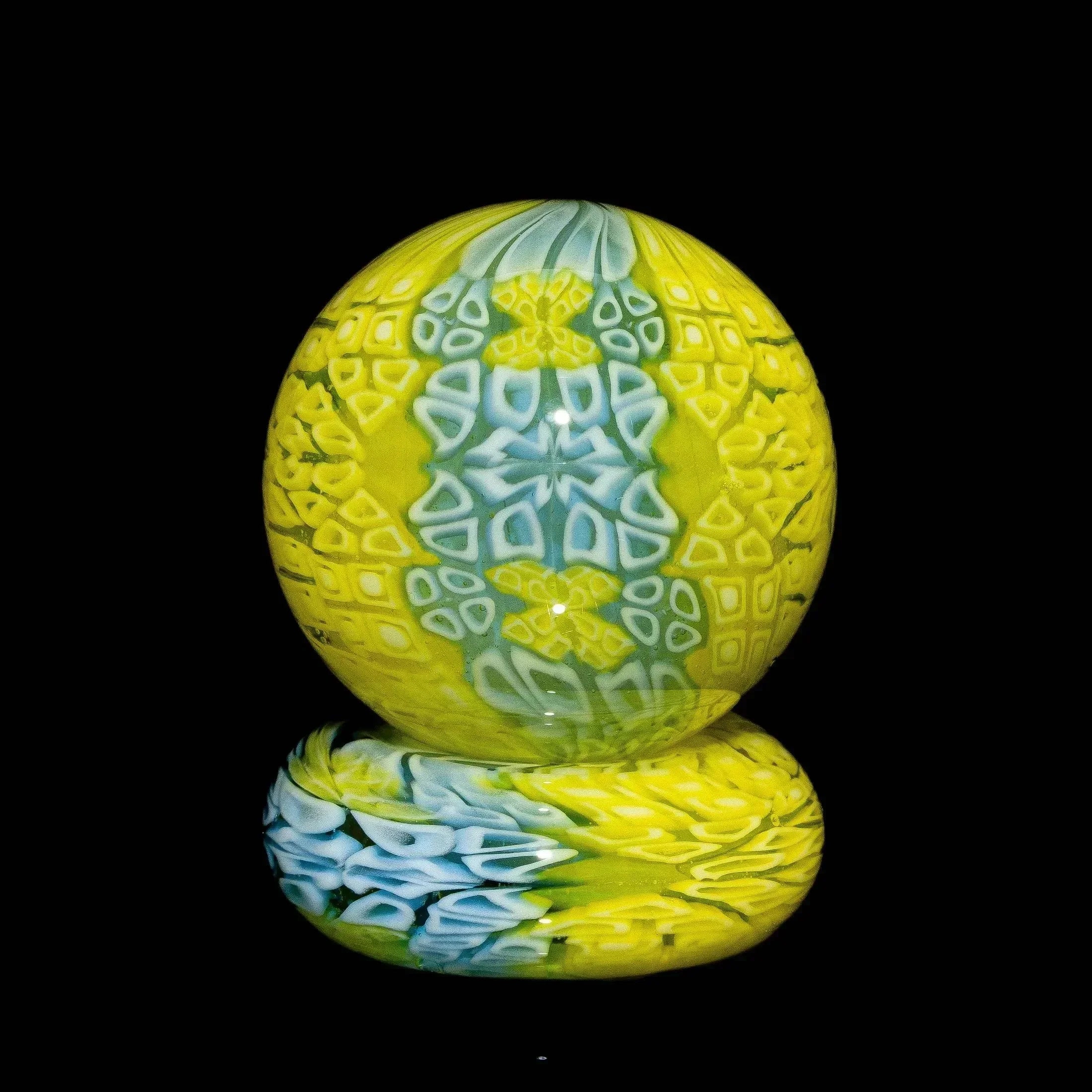 Intricate yellow and blue UV reactive glass marble with patterned design on black background
