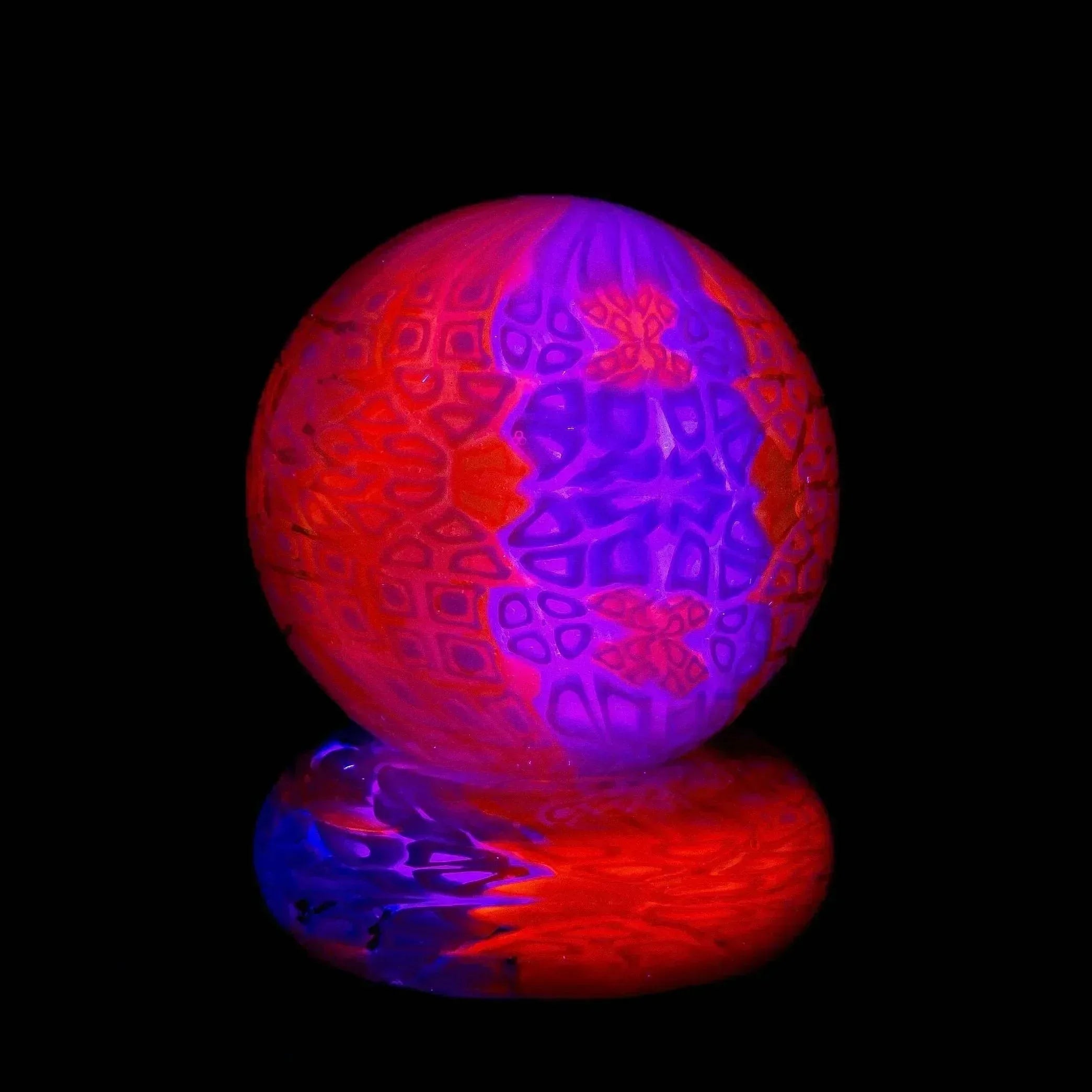 UV reactive glass marble with intricate purple and red pattern design on black background.