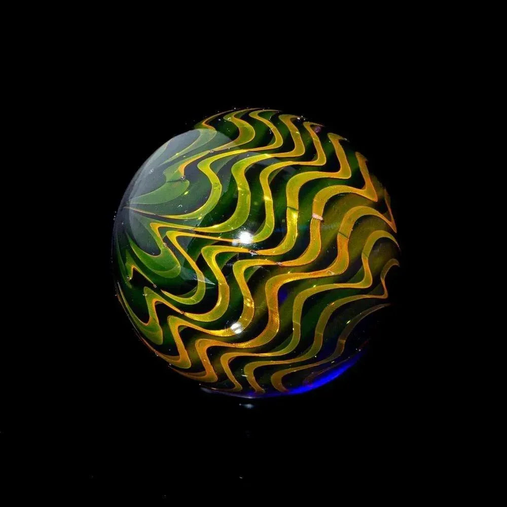 Hand-blown glass marble with yellow and green raked fume pattern, mirror finish, on black background.