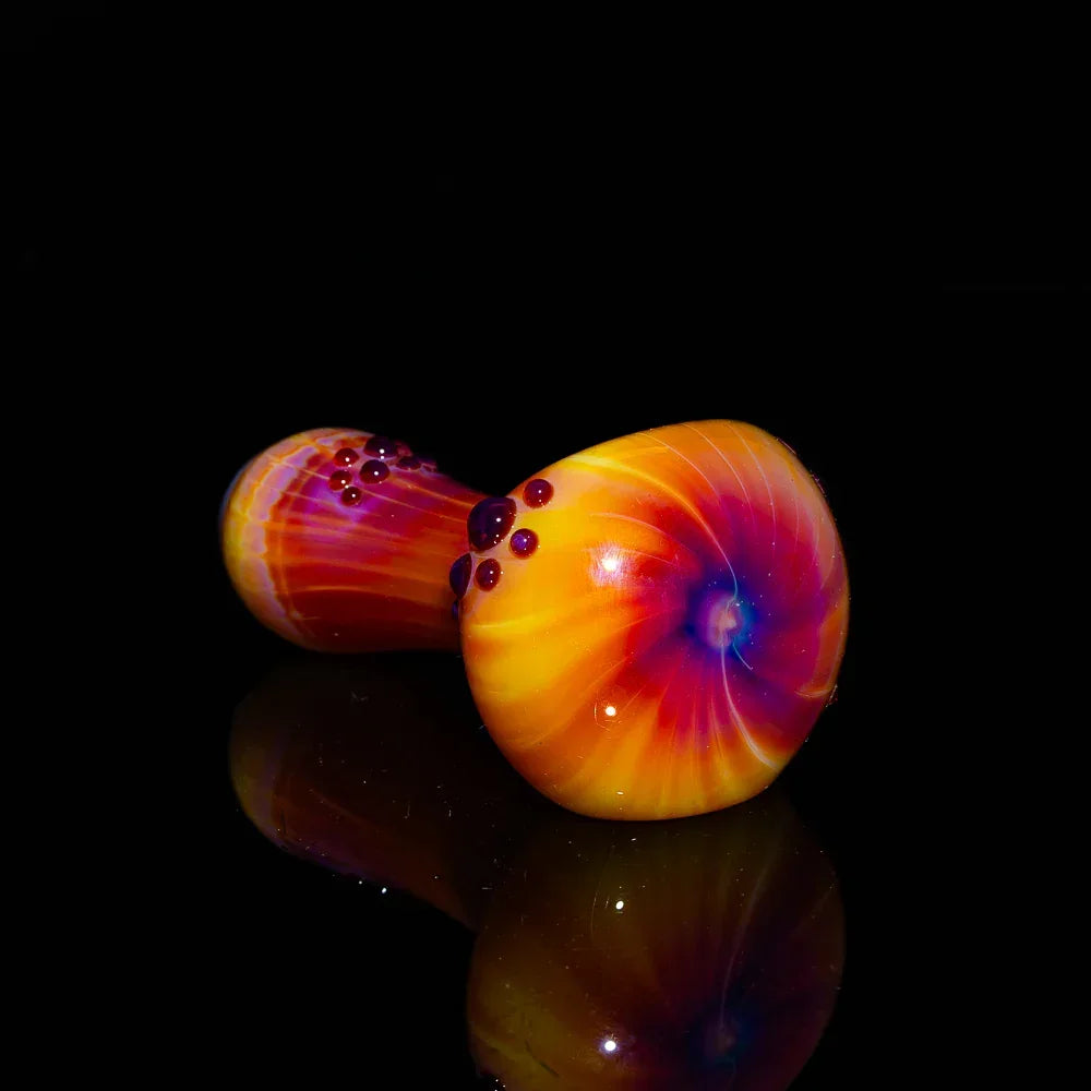 Hand-blown glass spoon pipe with vibrant orange, purple, and yellow swirl design on black background