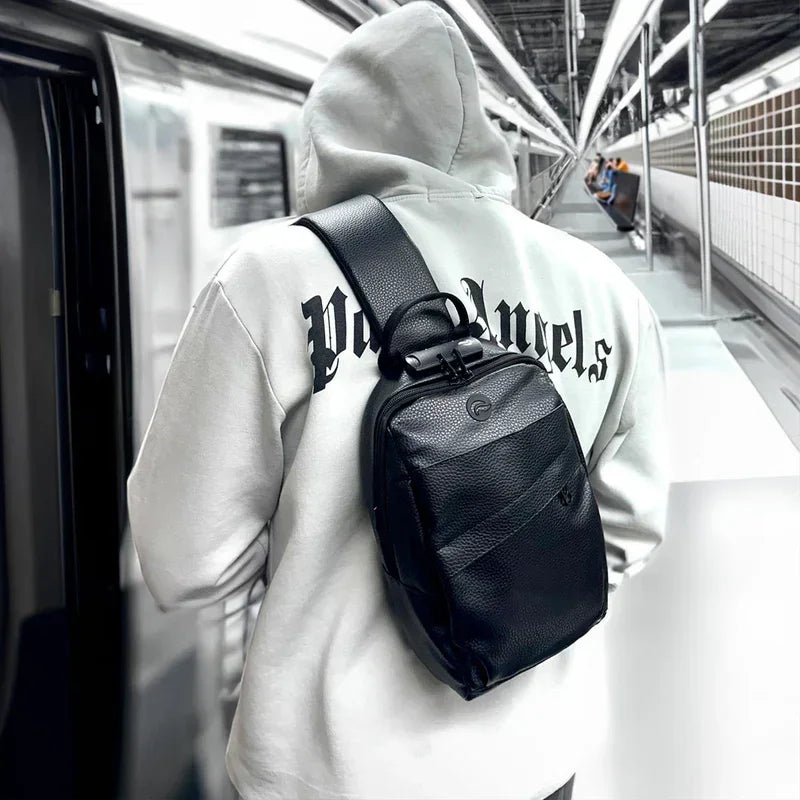 Man in subway wearing black leather crossbody sling bag and hoodie with gothic lettering.